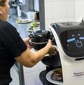 Eine Frau in einer Restaurantküche belädt einen Roboter mit Speisen.