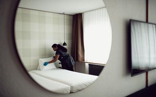 Person arbeitet in einem Hotelzimmer und deckt das Bett