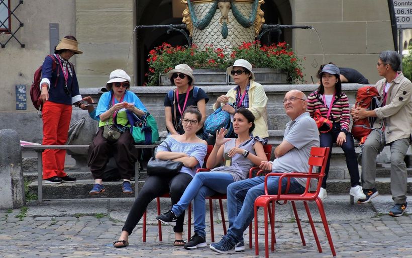Touristen sitzen auf Bänken und Stühlen auf dem Münsterplatz in Bern