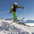 Ein Kind springt in voller Skimontur über eine kleine Schneeschanze.l