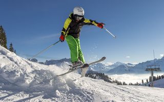 Ein Kind springt in voller Skimontur über eine kleine Schneeschanze.l