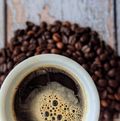 Eine Tasse schwarzer Kaffe ist umgeben von Kaffeebohnen